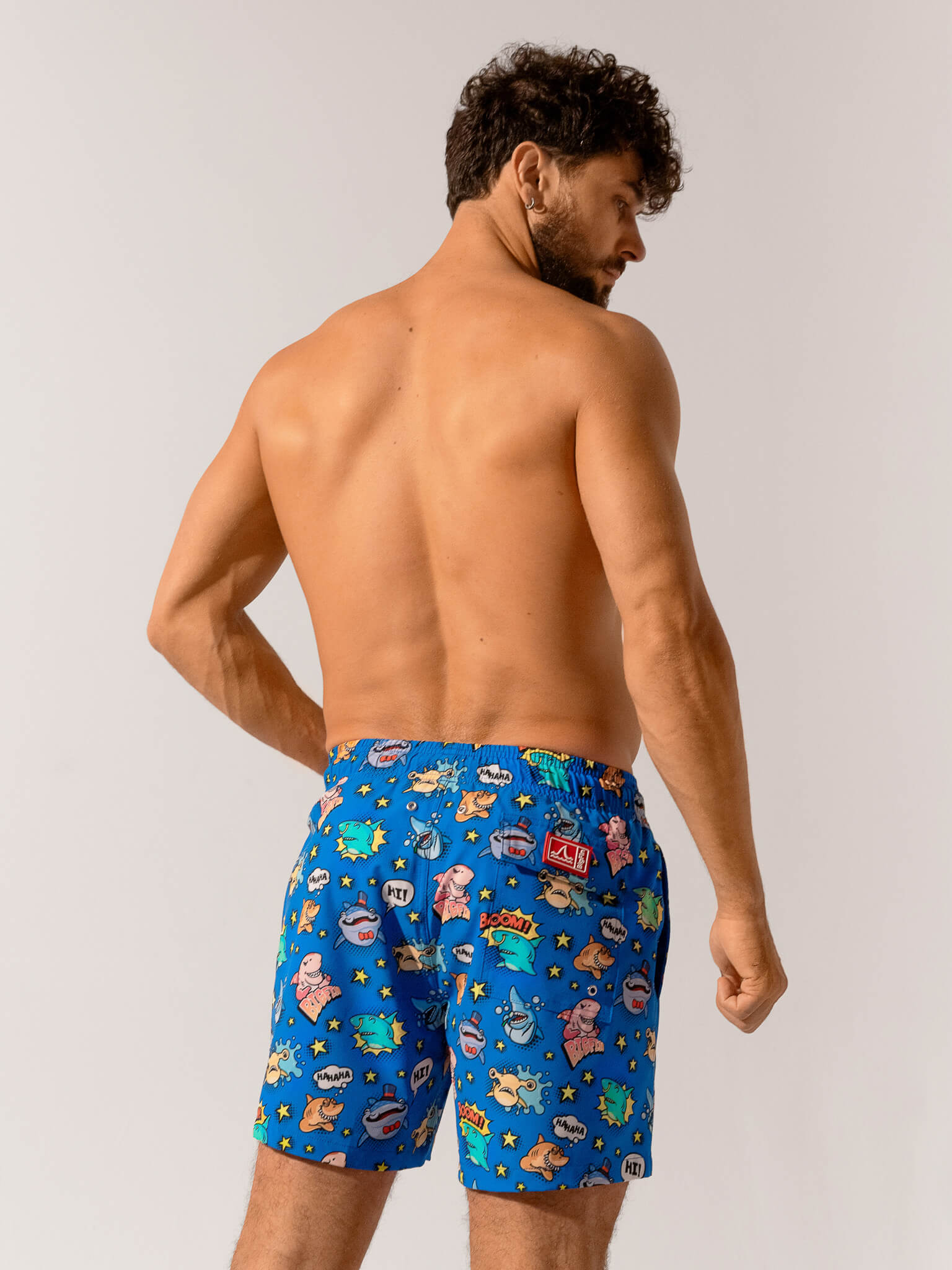 Man wearing blue swim shorts with cartoon character pattern on a plain background