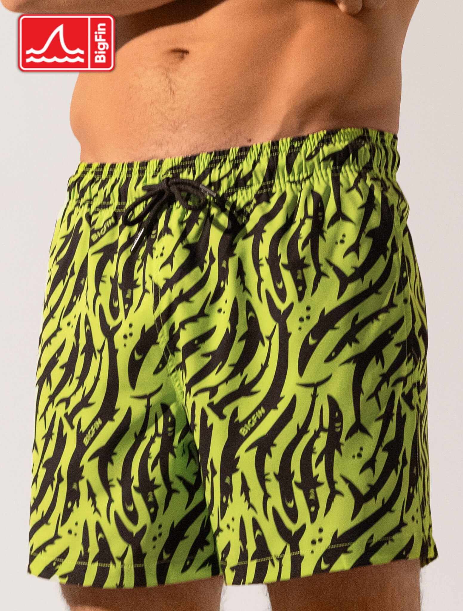 Green and black patterned swim shorts worn by a person on a white background, with BigFin logo.