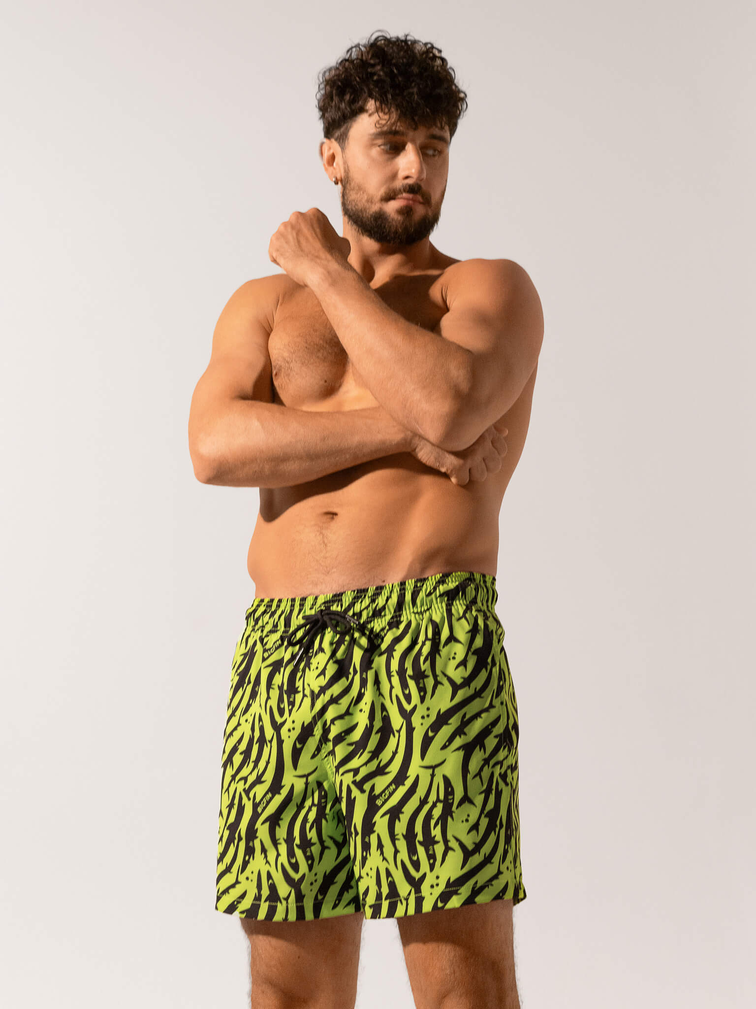 Man wearing green and black patterned swim shorts on a white background