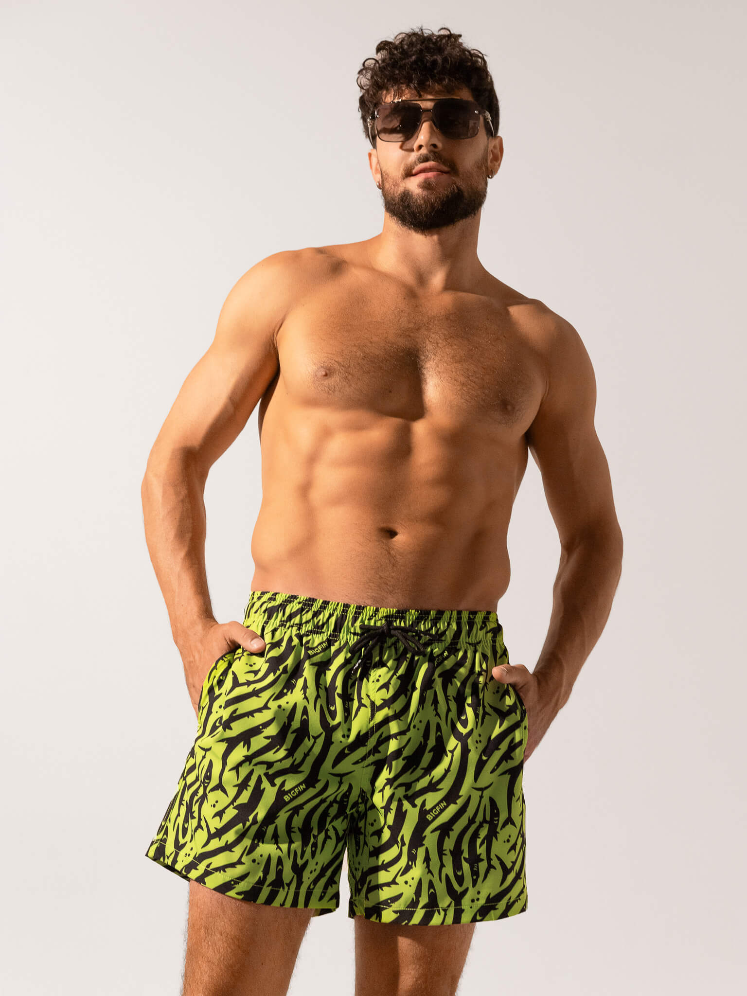 Man wearing green and black patterned swim shorts on a plain background