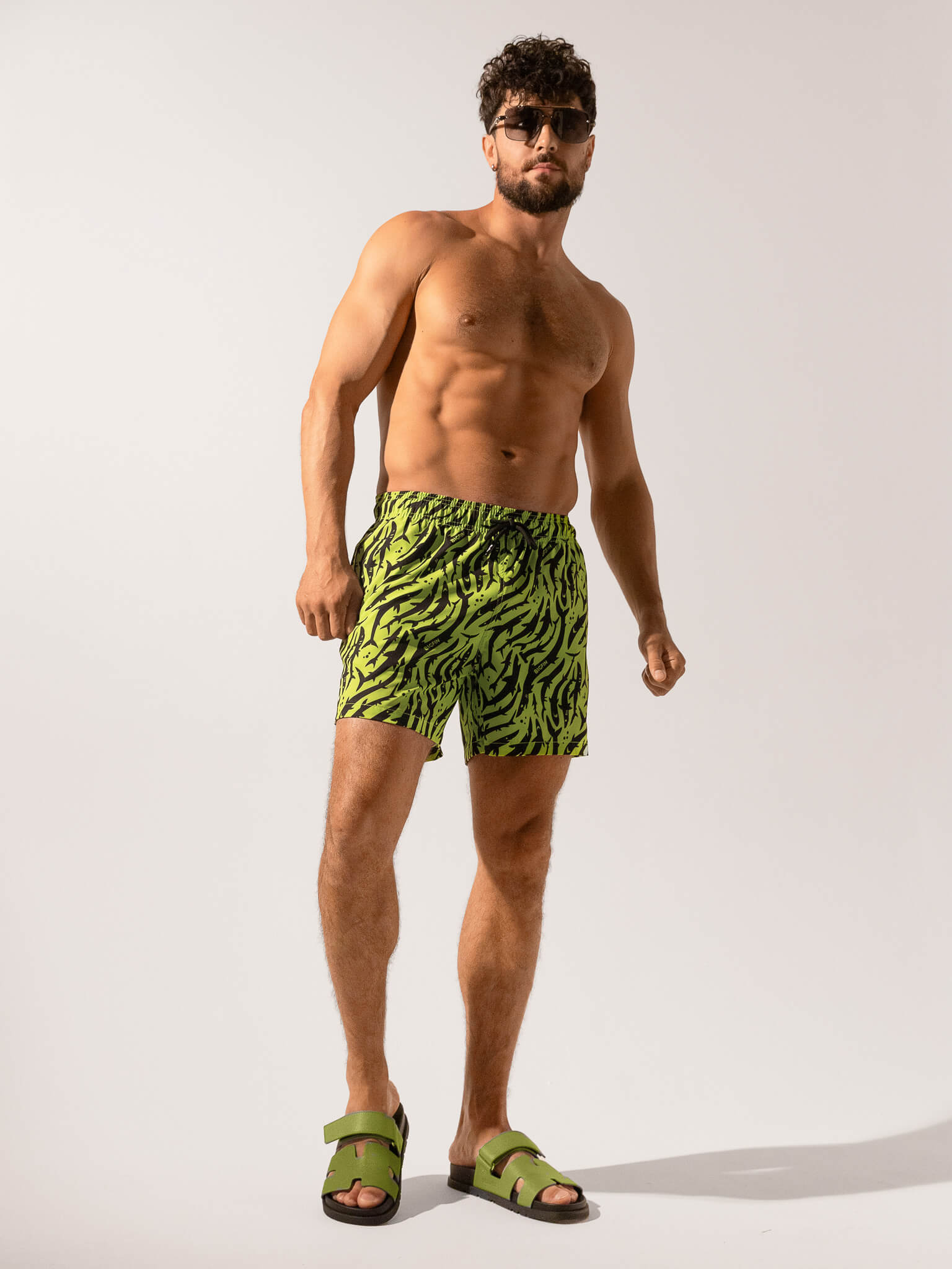 Man wearing green patterned swim shorts on a white background