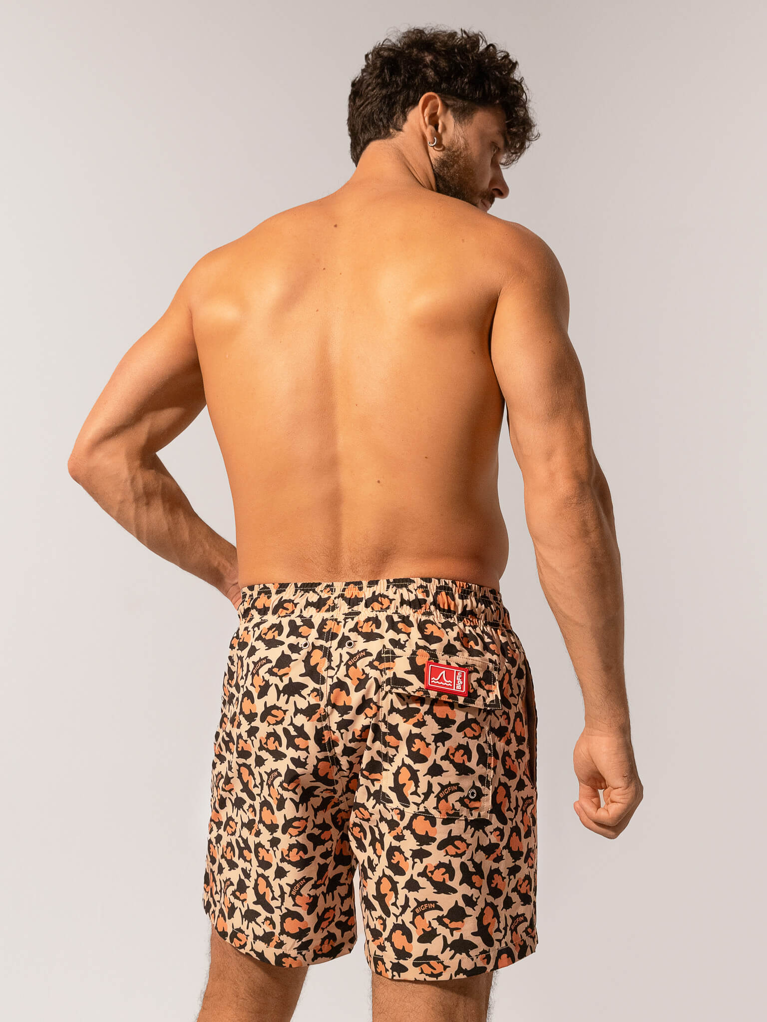 Man wearing leopard print swim shorts with a red logo on a plain background