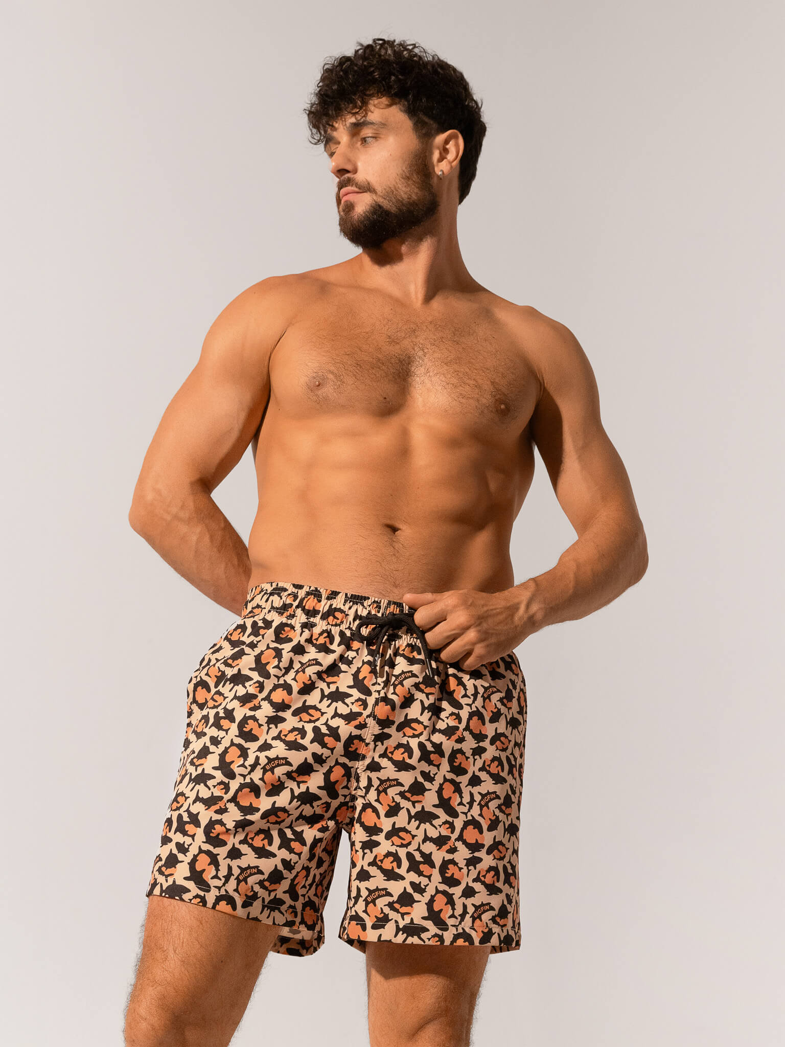 Man wearing leopard print swim shorts against a plain background
