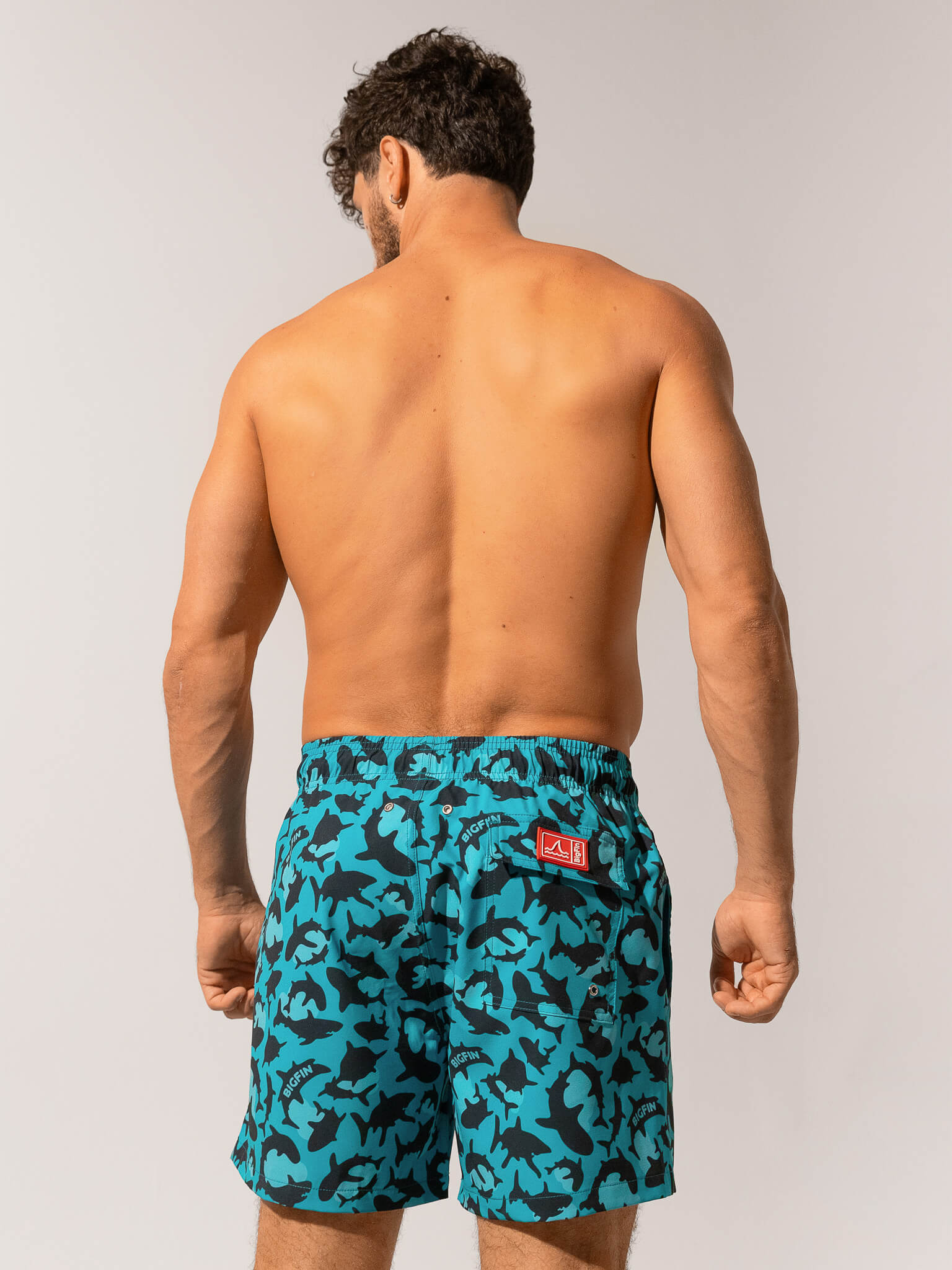 Man wearing blue camouflage swim shorts with a red logo on a light gray background