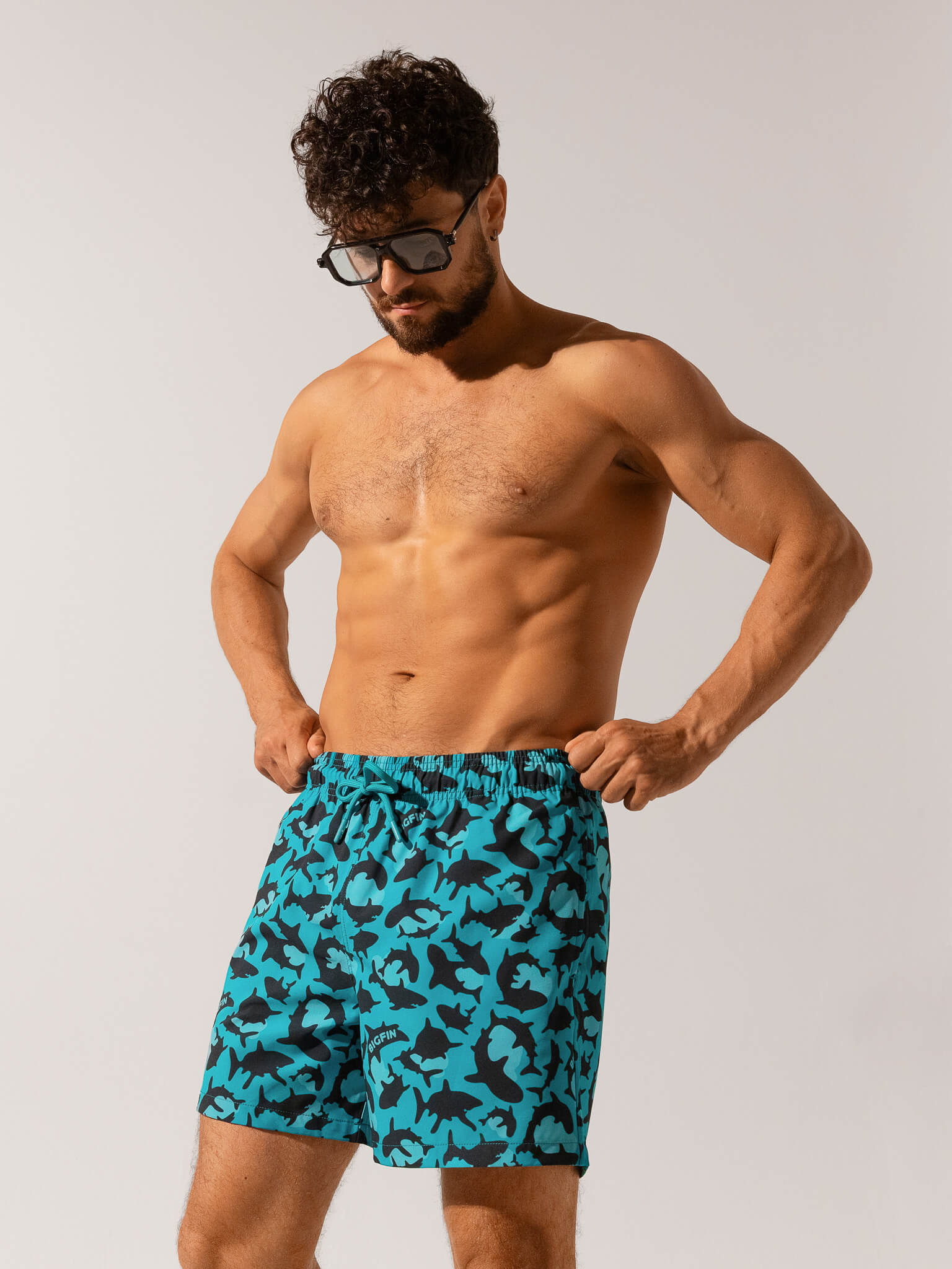 Man wearing blue camouflage swim shorts against a plain background