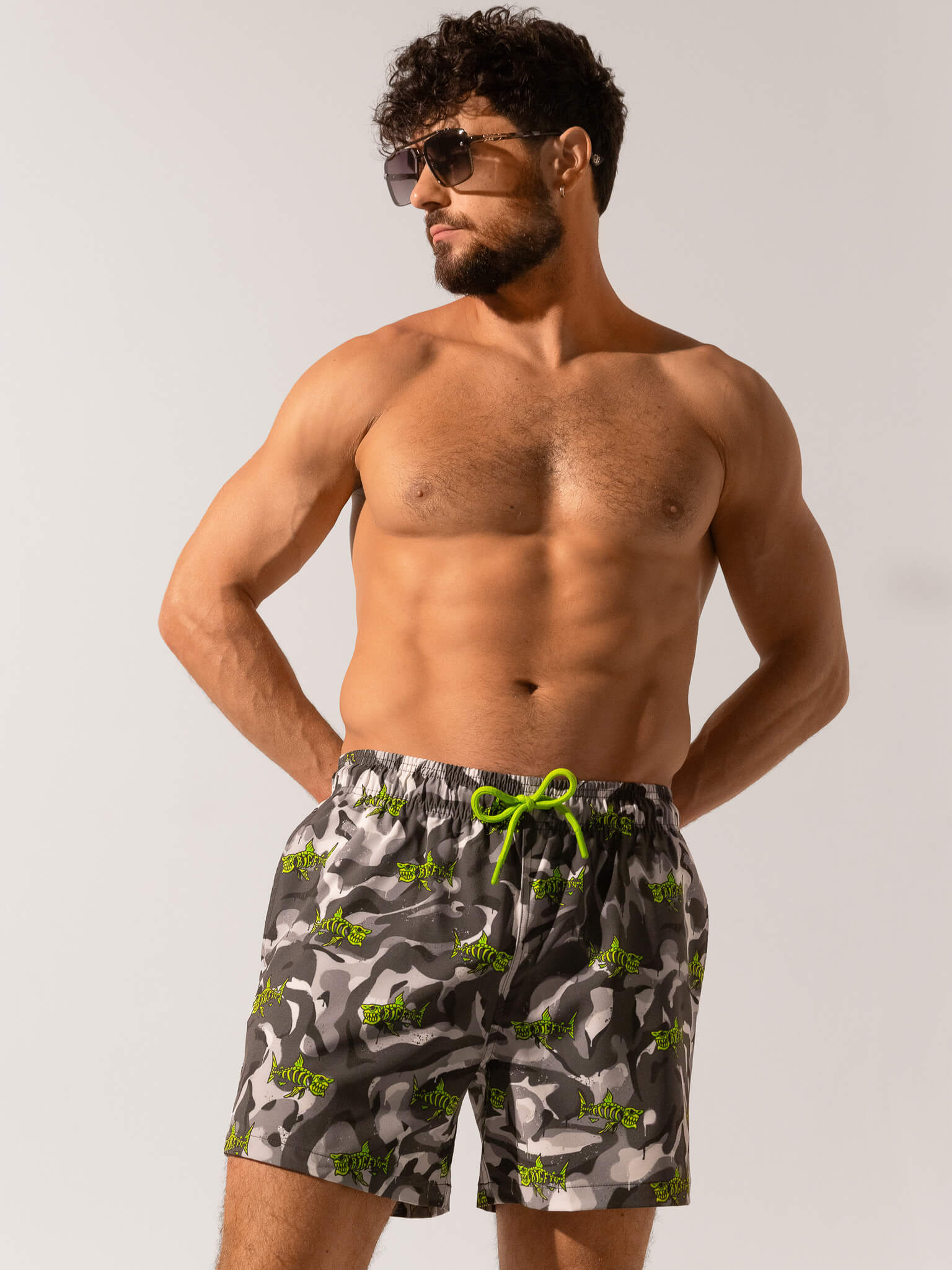 Man wearing camouflage swim shorts with a green drawstring on a plain background
