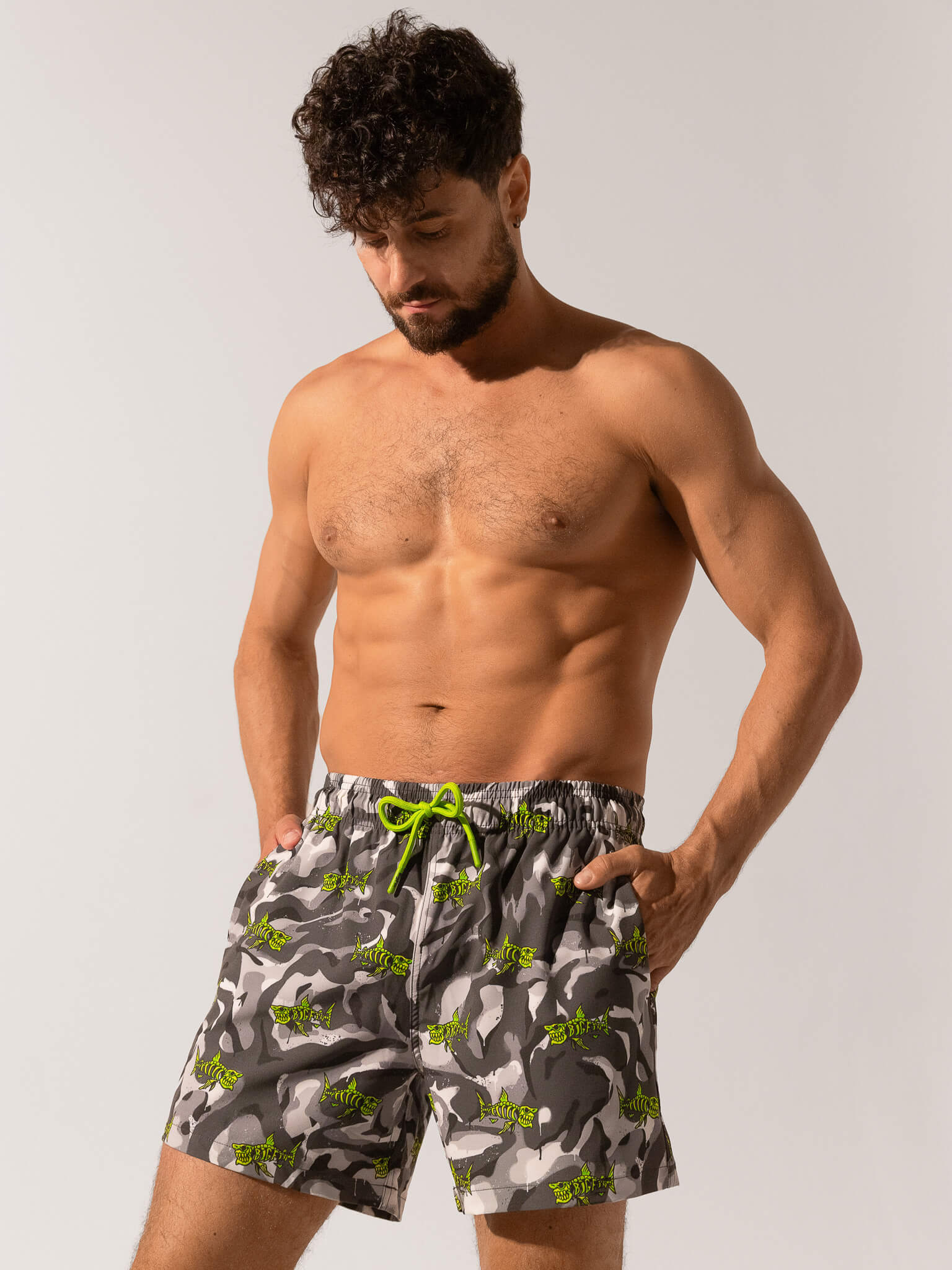 Man wearing camouflage swim shorts with a green drawstring on a plain background