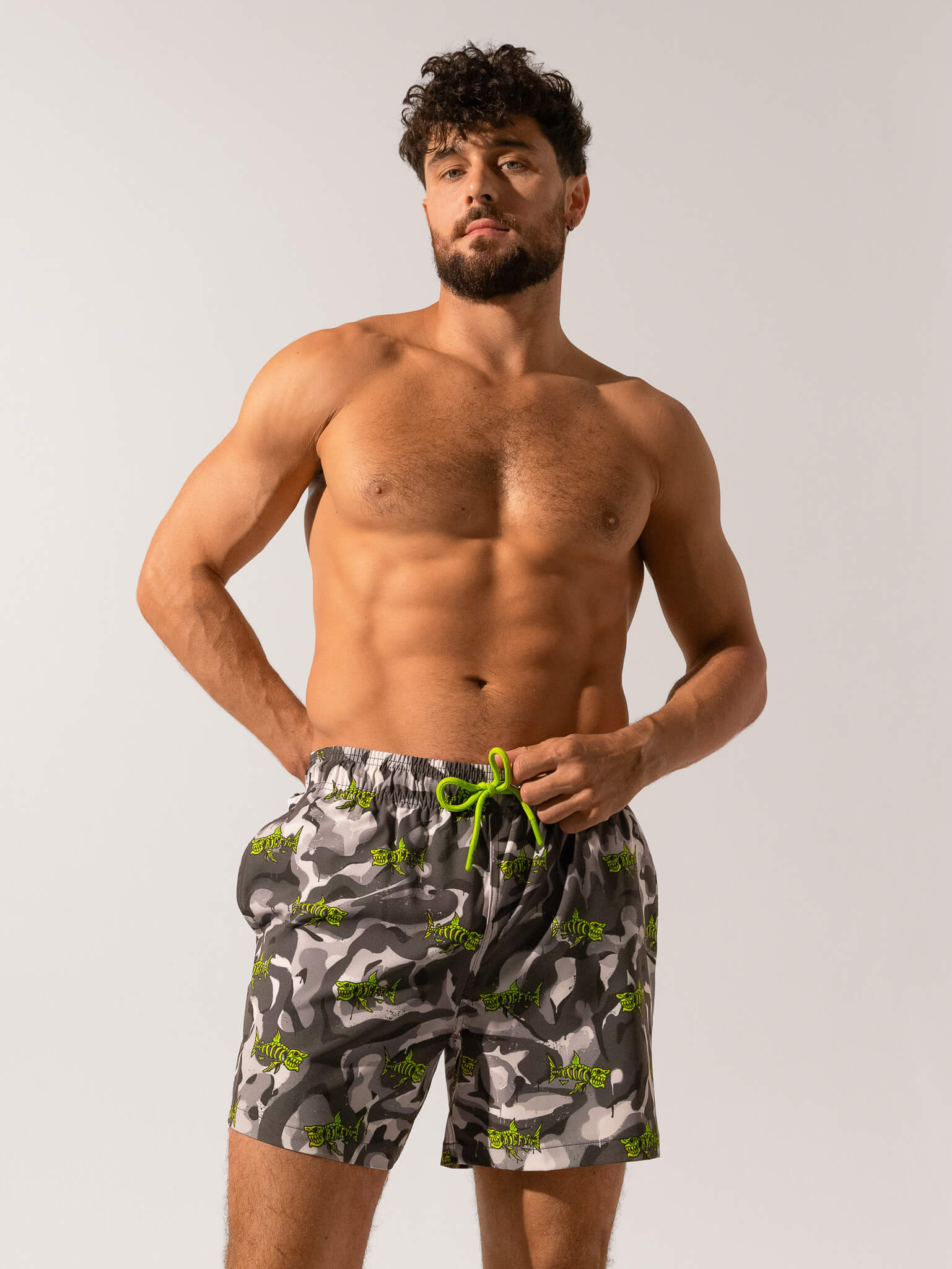 Man wearing camouflage swim shorts with a green drawstring on a plain background
