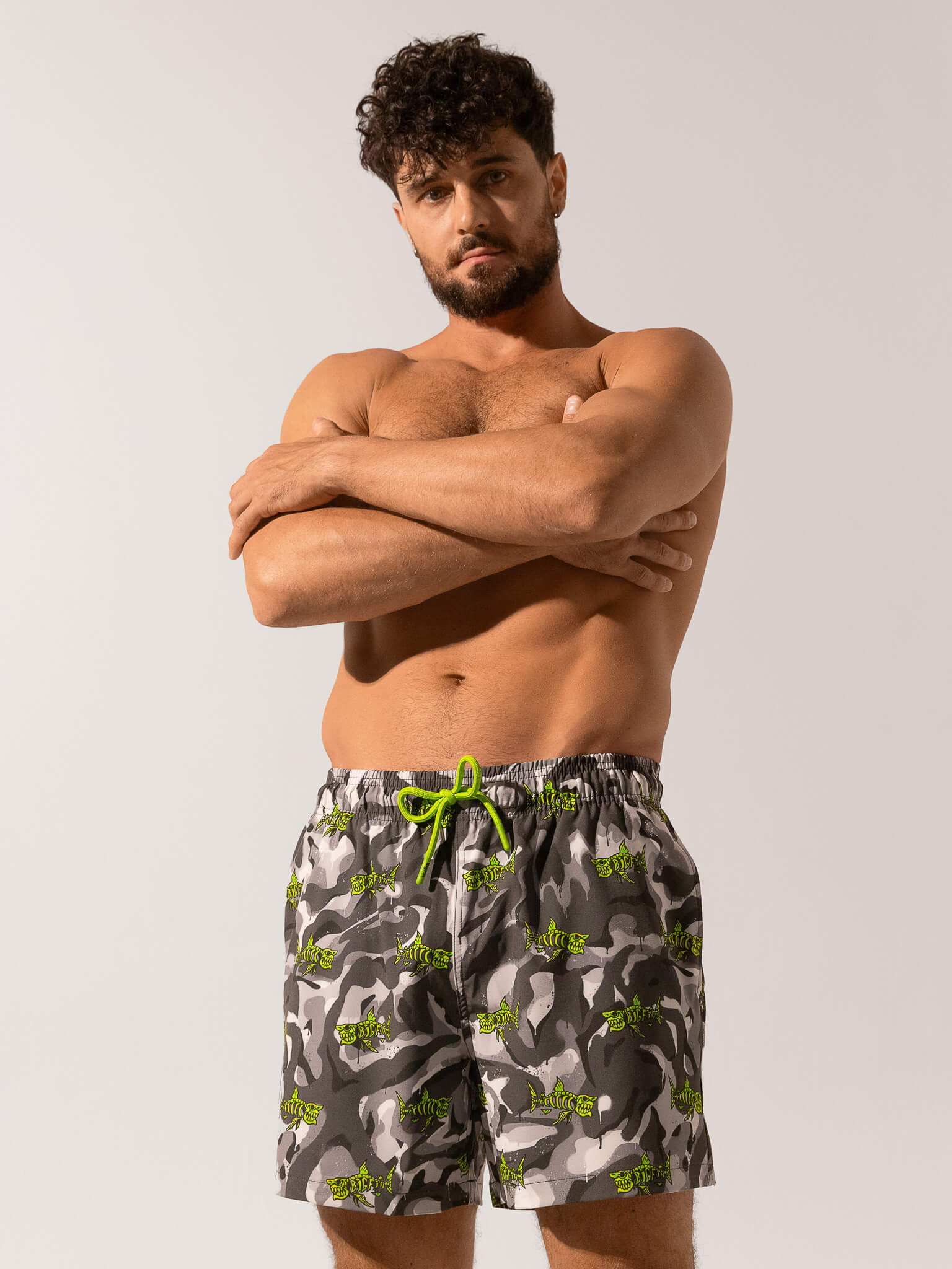 Man wearing camouflage swim shorts with a green drawstring on a plain background