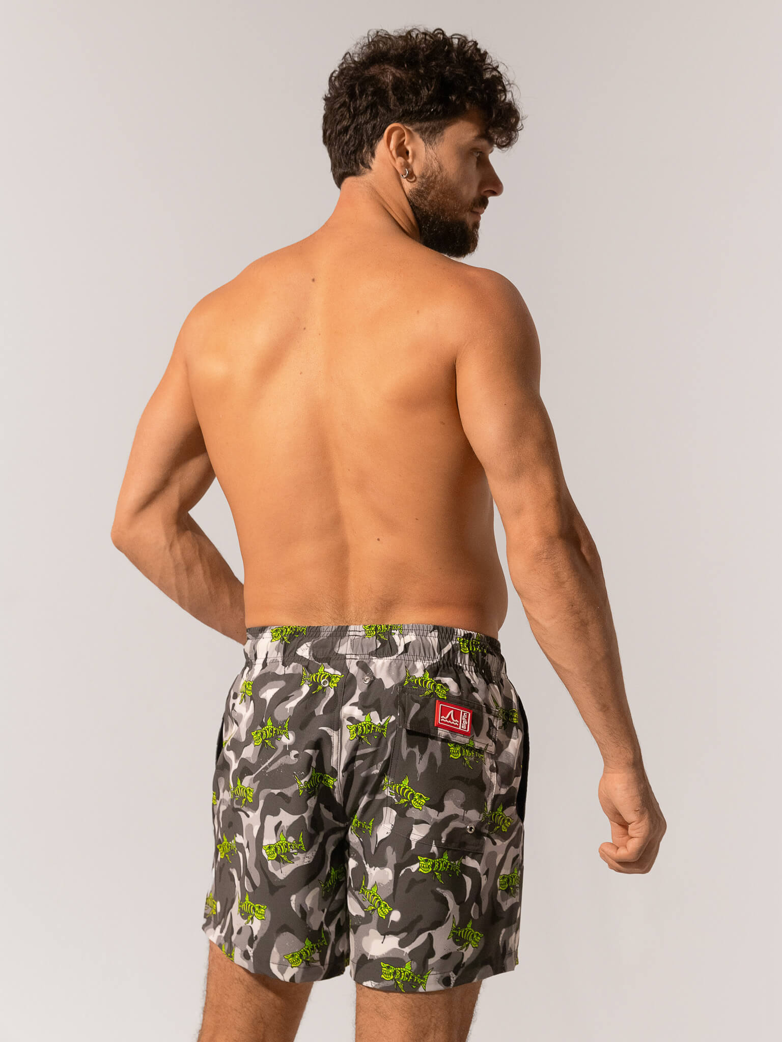 Man wearing camouflage swim shorts with a brand logo on a plain background