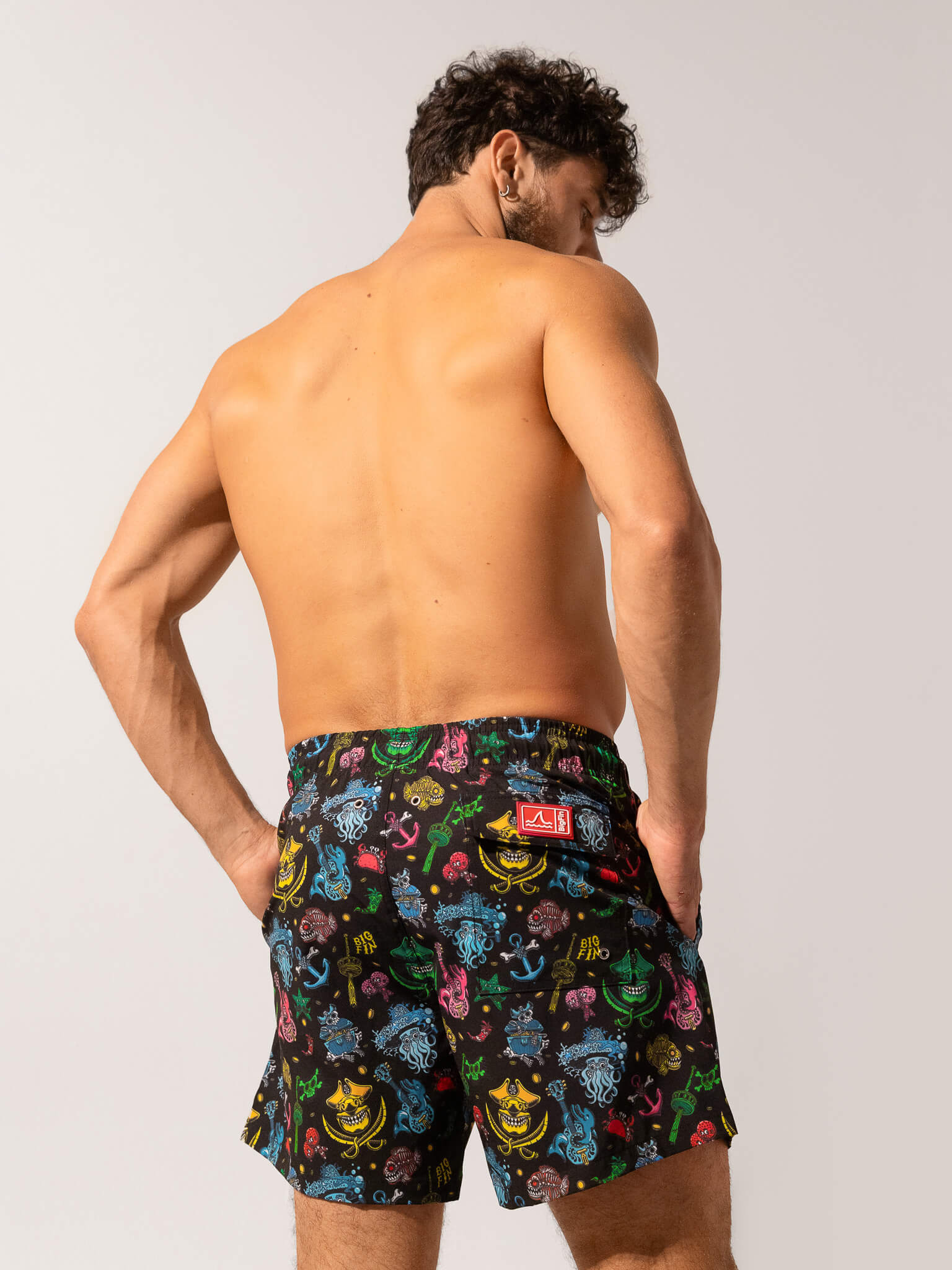 Man wearing colorful patterned swim shorts on a plain background