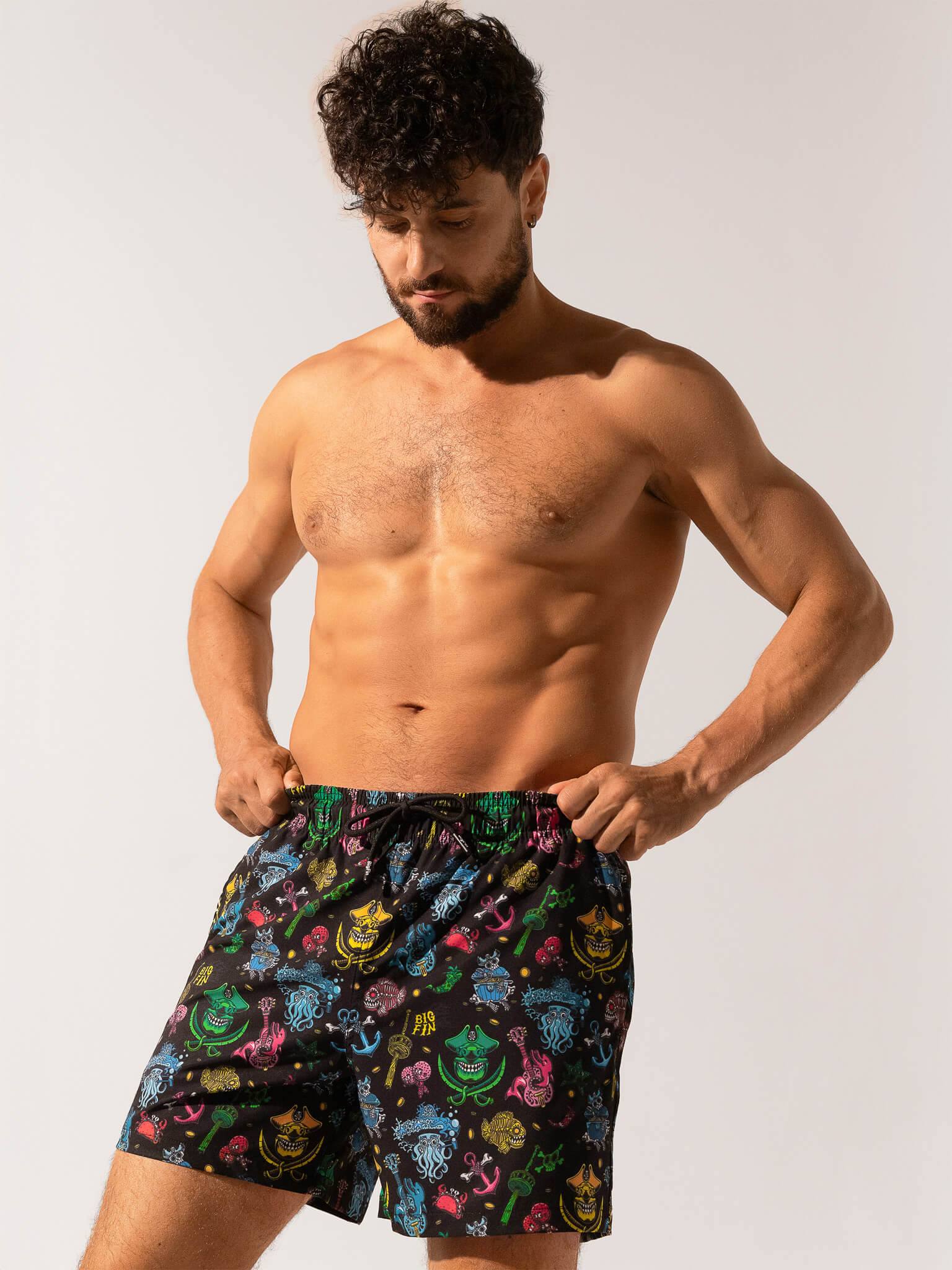 Man wearing colorful patterned shorts on a plain background