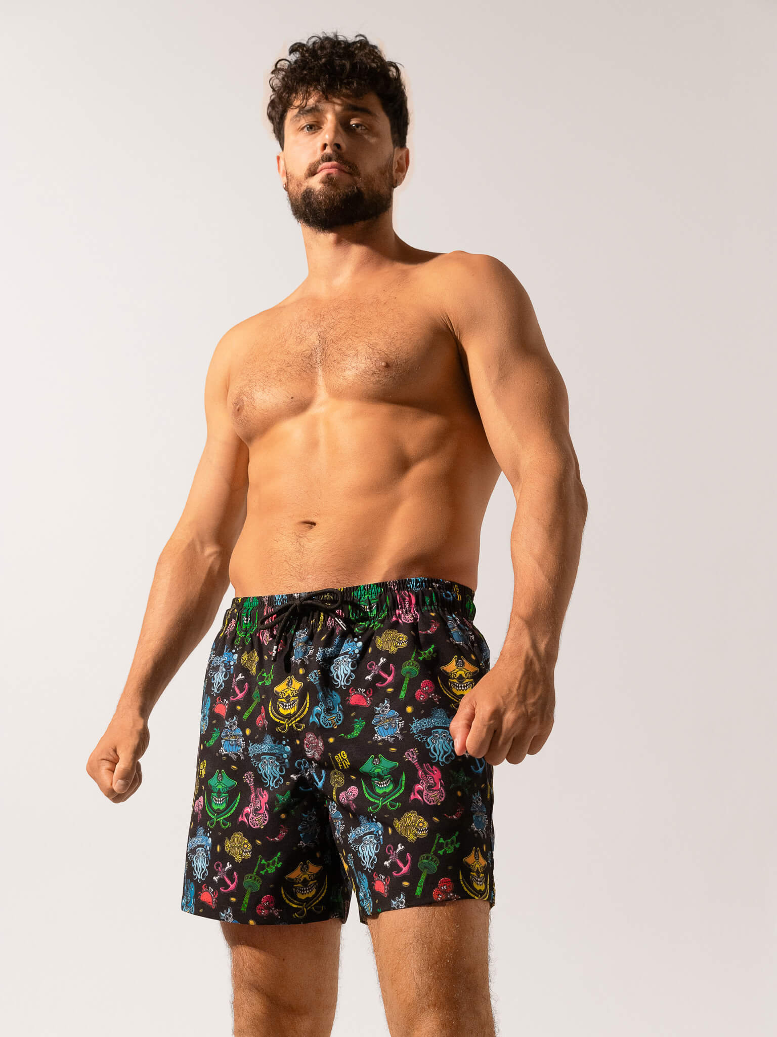 Man wearing colorful patterned swim shorts on a plain background