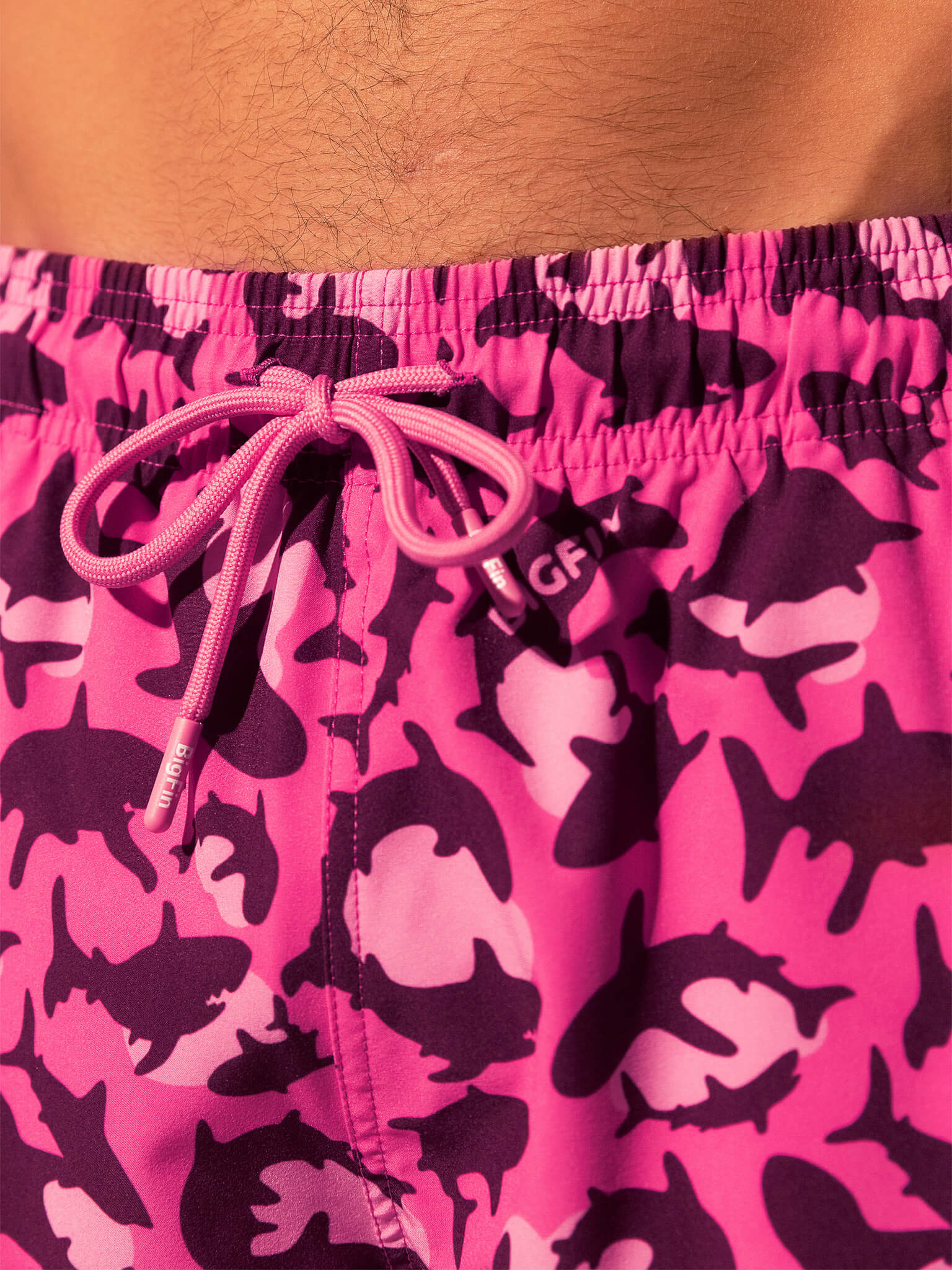 Pink swim shorts with shark pattern and drawstring on a pink background
