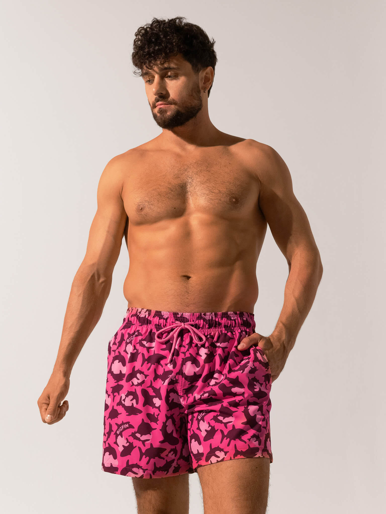 Man wearing pink camouflage swim shorts against a plain background