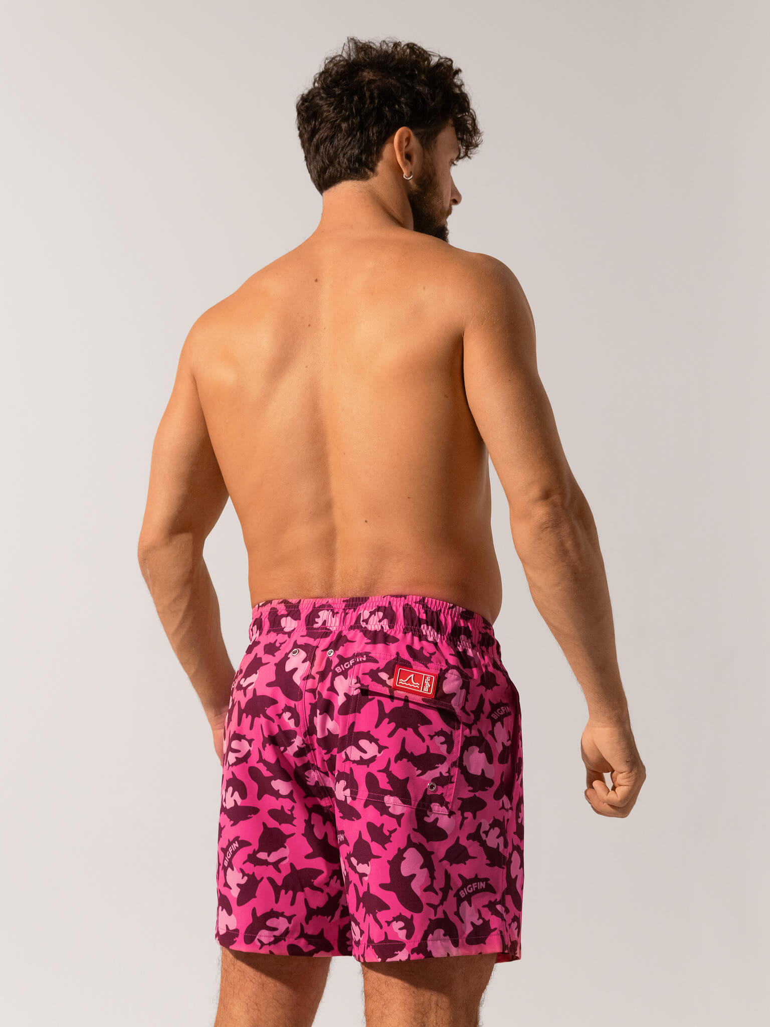 Man wearing pink camouflage swim shorts on a white background