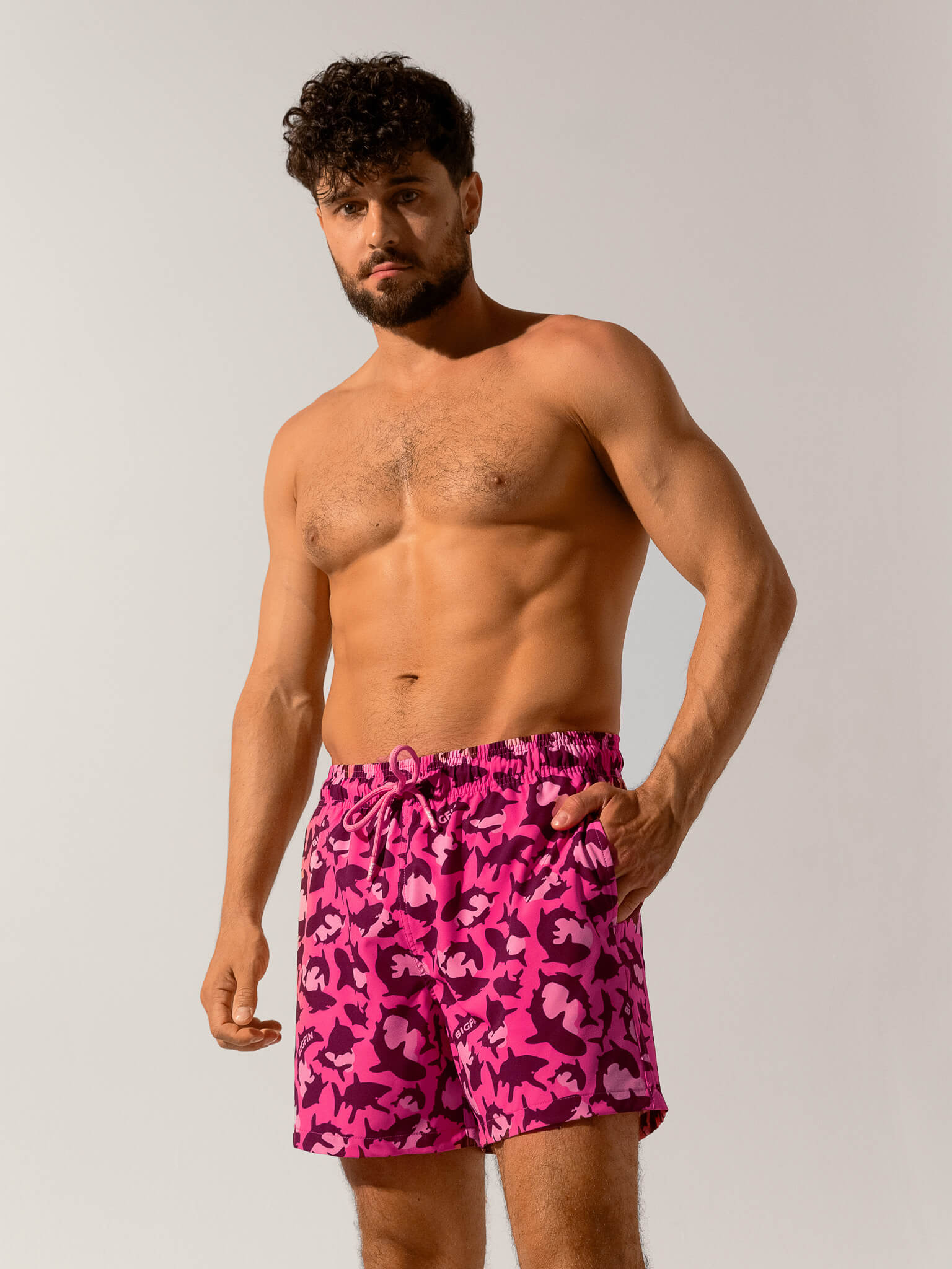 Man wearing pink swim shorts with a pattern against a plain background