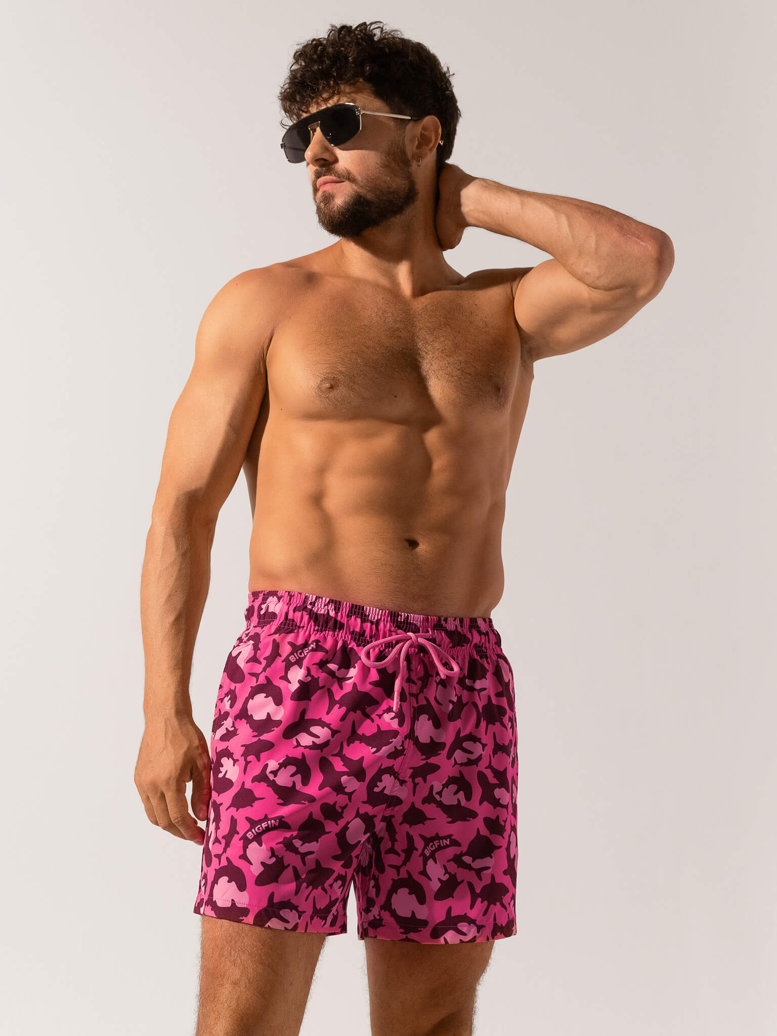 Man wearing pink camouflage swim shorts on a white background