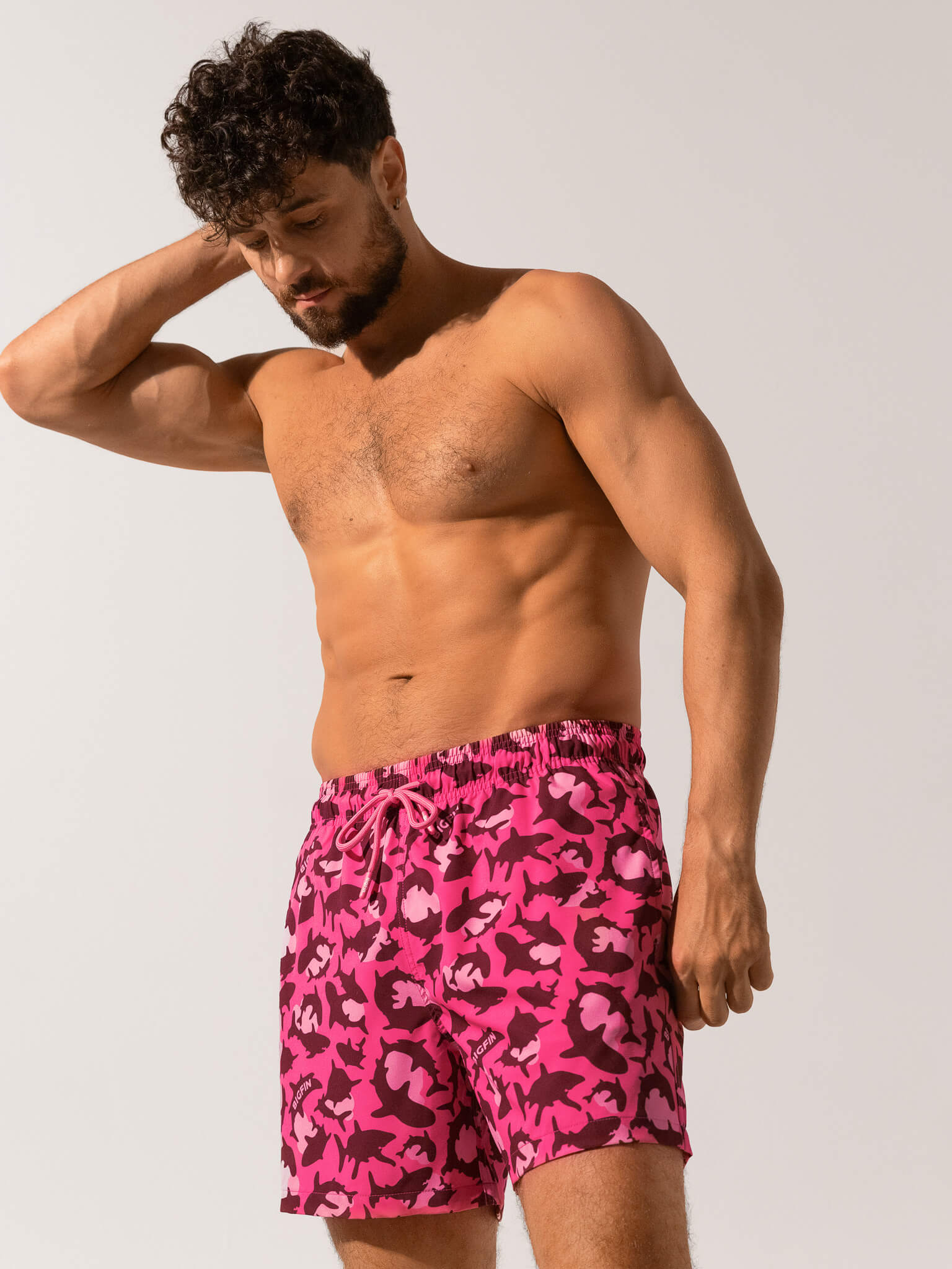 Man wearing pink camouflage swim shorts against a plain background